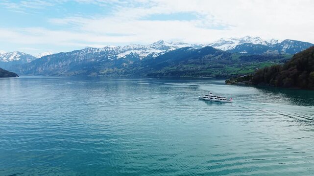 Aerial: white boat sailing on Thun Lake with snowy mountain during the day near Spiez, Canton of Bern, Switzerland, push in drone shot