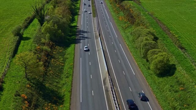 Drone flies above highway with cars moving through Mayenne fields