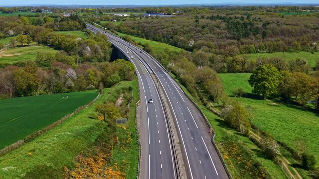 Drone flies above curved highway crossing Mayenne rural landscape