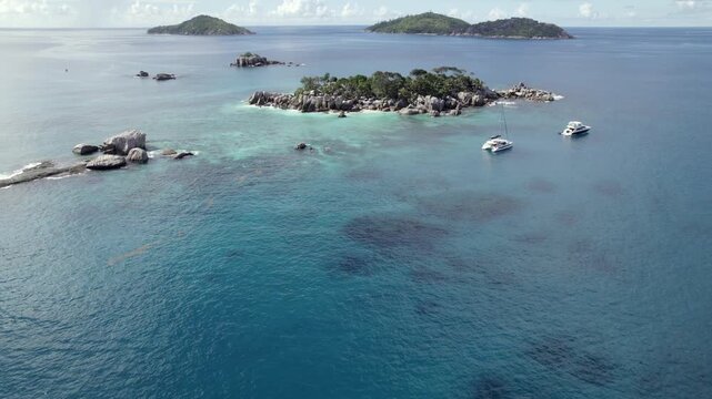 Drone heading to cocos island, docked catamarans and lux boat, lush untouched nature, granite stones, clear turquoise water, Big sister and small sister island at the back, Seychelles 001 30fps