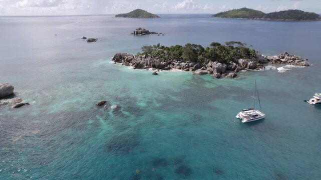 Drone heading to cocos island, docked catamaran and lux yacht, lush untouched nature, granite stones,clear turquoise water, Big sister and small sister island at the back, Seychelles 002 30fps