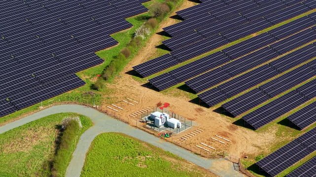 Aerial view of a large solar farm with rows of photovoltaic panels and an electrical substation on green fields in Nailstone, England, United Kingdom.