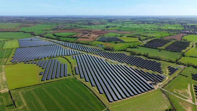 Aerial view of a large solar farm with rows of photovoltaic panels surrounded by green fields and hedgerows in Nailstone, England, United Kingdom.