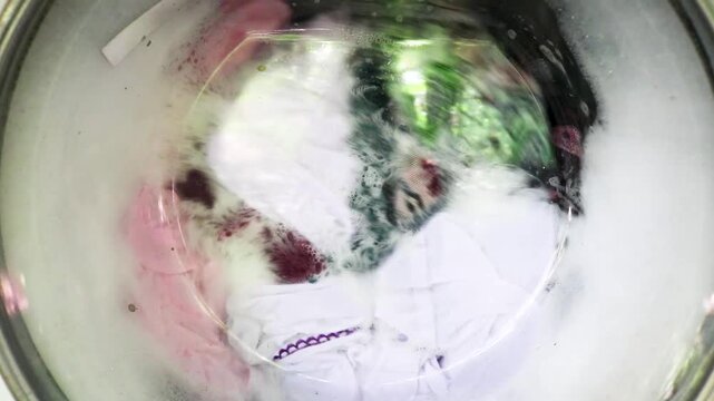 Close up of clothes being washed in a washing machine, seen through the outside glass. The washing machine shows the clothes and the foam being spun.