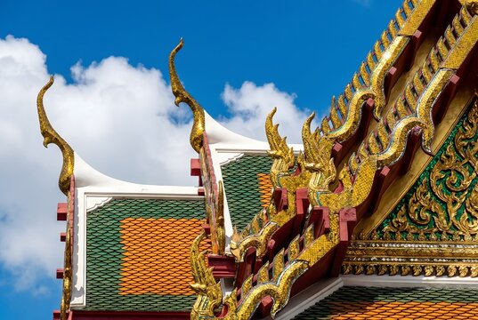 An extreme close-up architectural detail photograph of overlapping multi-tiered Thai temple roof eaves, showcasing intricate Chofa sky tassel finials in gilded bronze shaped as Garuda bird heads.