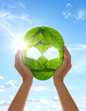 Hands holding a green leaf earth icon against a bright blue sky.