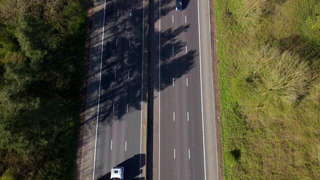 Aerial view of cars driving on the M1 motorway through wooded areas and green fields in Leicestershire, England, United Kingdom.