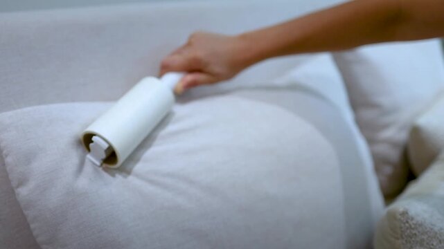 Hand Using Lint Roller to Clean Beige Pillow on Bed