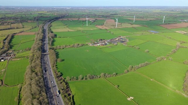 Aerial view of the M1 motorway with traffic passing through green fields and wind turbines in Leicestershire, England, United Kingdom.