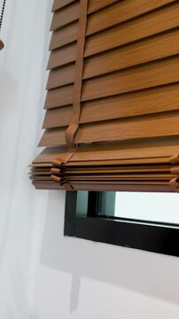 Hands Pulling Cord to Raise Wooden Venetian Blinds on White Wall