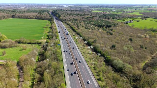 Aerial view of the M1 motorway with traffic flowing through lush green fields and dense woodland in Leicestershire, England, United Kingdom.