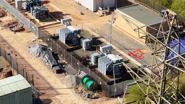 Aerial view of Coalville Substation featuring electrical transformers, power pylons, and utility buildings under bright sunlight in Coalville, England, United Kingdom.