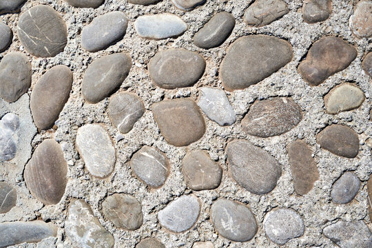 Close-up texture of smooth river stones embedded in concrete. Durable outdoor pavement for architectural, landscaping, and construction concepts