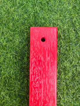 Red painted wooden plank placed on green grass, creating a bold contrast between natural texture and man-made material