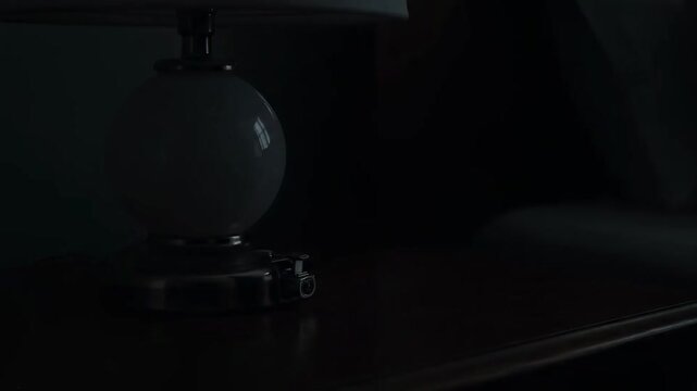 Evening Ambiance: Person Turning On And Off A Bedside Lamp In A Dark Room
