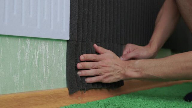 Homeowner installs foam for noise reduction. Applying acoustic panels and strips to improve room sound. Person carefully attaches insulation panels and soundproof strips to walls