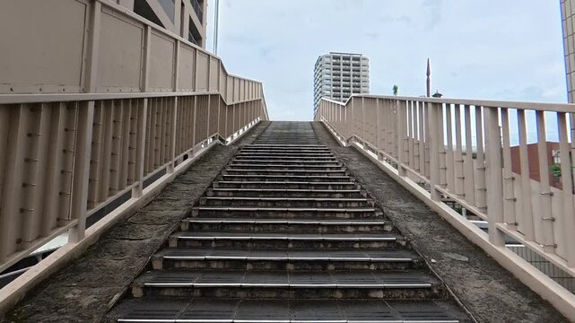 POV walking up pedestrian bridge stairs in light rain, raindrops on steps during a moody day