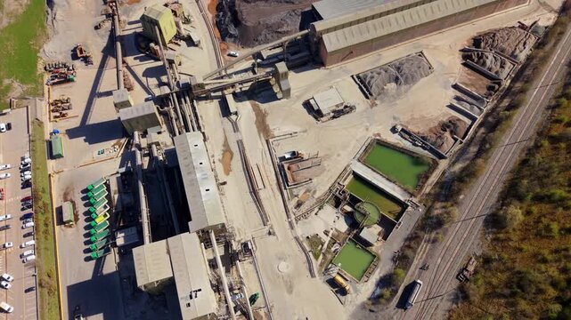 Aerial view of Cliffe Hill Quarry with industrial buildings, conveyor systems, and green settling ponds in Ellistown, England, United Kingdom.