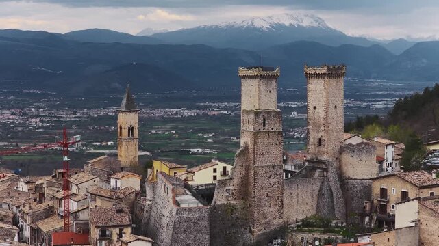Aerial view of the medieval Caldora Castle with its stone towers and the historic rooftops of the village against snow-capped mountains in Pacentro, Abruzzo, Italy.