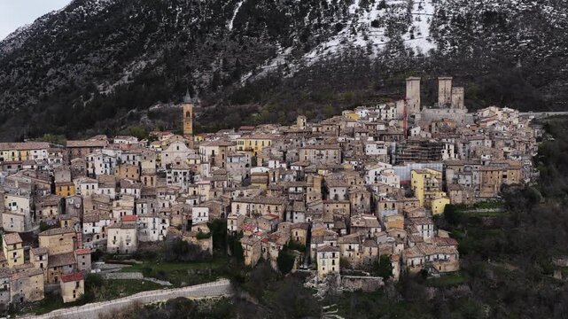 Aerial view of the historic stone houses and medieval towers of Pacentro nestled against snow-capped mountains in Pacentro, Abruzzo, Italy.