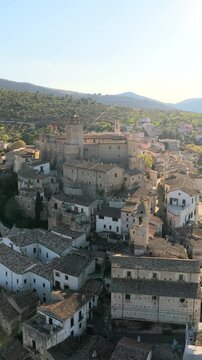 Aerial view of the historic Castello Piccolomini surrounded by stone houses and rolling green hills in Capestrano, Abruzzo, Italy.