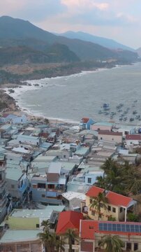 A coastal village iof  Bai Xep, Quy Nhon, Vietnam. shows signs of damage, with boats in the choppy sea and a telecommunications tower overlooking the scene.