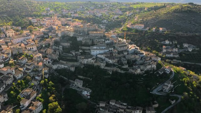 Aerial view of the historic Castello Piccolomini and stone houses of the hilltop village surrounded by green hills in Capestrano, Abruzzo, Italy.