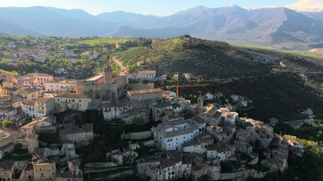 Aerial view of the historic Castello Piccolomini and stone houses of Capestrano nestled among the green hills and mountains of the Abruzzo region, Capestrano, Abruzzo, Italy.