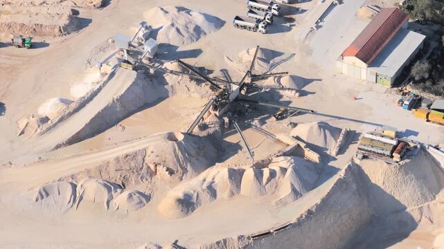 Aerial view of a sand quarry with conveyor belts, large piles of sand, and industrial trucks in Capestrano, Abruzzo, Italy.