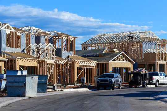 Two-story homes under construction in a new residential development with framing and roofing in progress, representing housing growth and suburban building activity