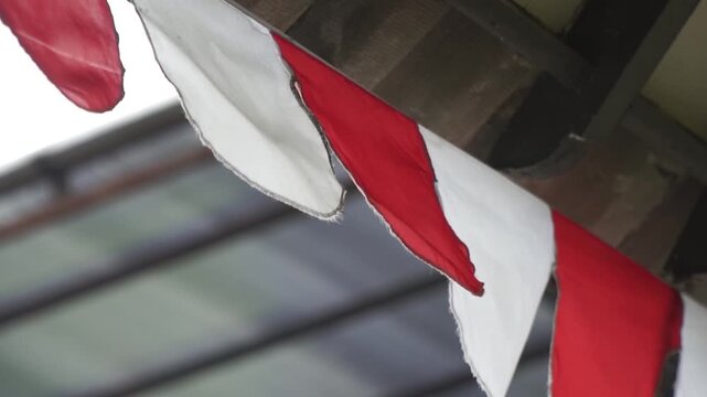Red and white Indonesian bunting flags hanging on a wooden roof. Traditional decoration for Independence Day celebration (17 Agustus) in a local neighborhood. Symbol of nationalism and festivity.