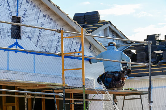 Construction worker installing metal lath over building wrap on a residential structure prior to exterior plaster application, representing stucco preparation and exterior wall assembly