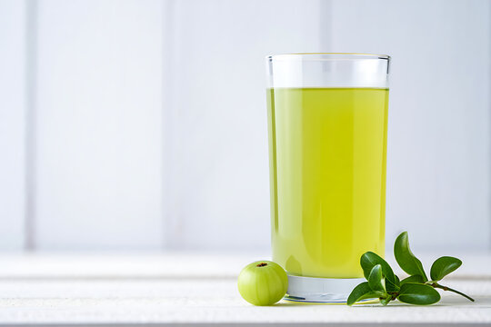 Tall glass of green amla juice with amla fruit and leaves drink