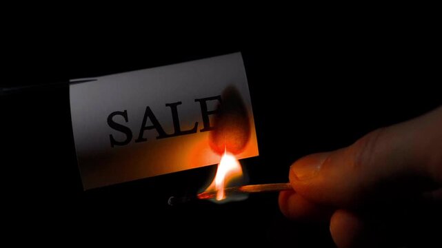 Word SALE on paper being set on fire with match close-up on black background