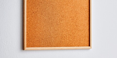Fototapeta premium Simple wooden framed corkboard hanging on a textured white wall