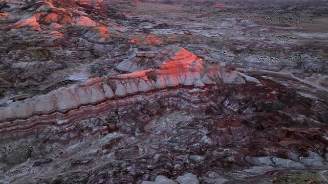 Aerial view of the colorful bentonite hills and rugged badlands terrain glowing under the warm sunset light in Hanksville, Utah, United States.