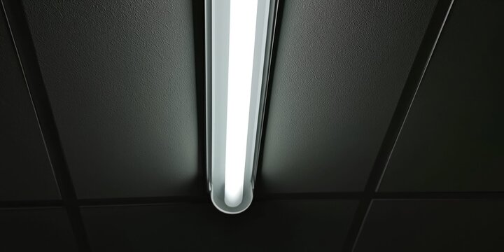 Modern fluorescent tube light fixture illuminating a dark ceiling grid