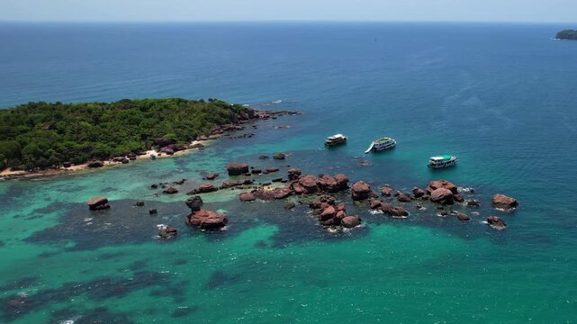 Stunning aerial drone video of Gam Ghi Island on Phu Quoc in south Vietnam with turquoise blue water and vivid coral reefs with tourists snorkeling and jumping off the boats on a hot sunny day