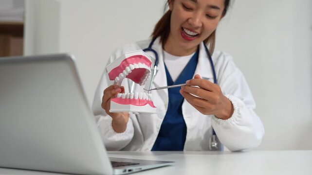 dentist video consultation, communicates with patient via an online conference, uses laptop, diagnoses, recommended and tooth models and analyzing dental treatments, and also answers questions.