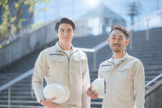 A portrait of a worker holding a helmet; a construction site and growth; a building in the background; an image of looking up toward the future and hope; two people in work clothes looking directly at