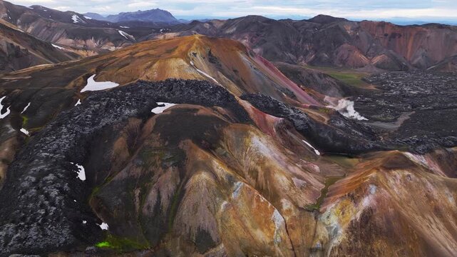 Aerial view of the vibrant rhyolite mountains with geothermal steam and dark lava fields in Landmannalaugar, Rangarthing ytra, Iceland.