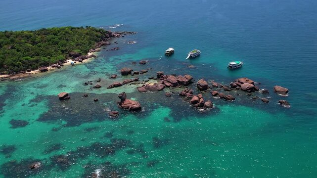 Stunning aerial drone video of Gam Ghi Island on Phu Quoc in south Vietnam with turquoise blue water and vivid coral reefs with tourists snorkeling and jumping off the boats on a hot sunny day