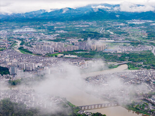 Obraz premium An aerial view captures the historic Huizhou Ancient City in She County of Anhui Province in China with mist flowing over the river and traditional buildings surrounded by mountains