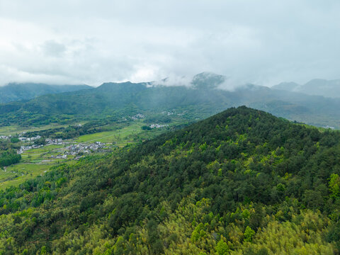 A high angle view captures the lush green landscape surrounding the historic and ancient Hongcun village in Yixian County of Anhui province in China under a soft cloudy sky
