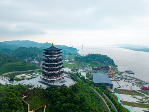 An aerial view of a traditional pagoda standing on a green hill overlooking the river and cityscape in Jiujiang China during a cloudy day