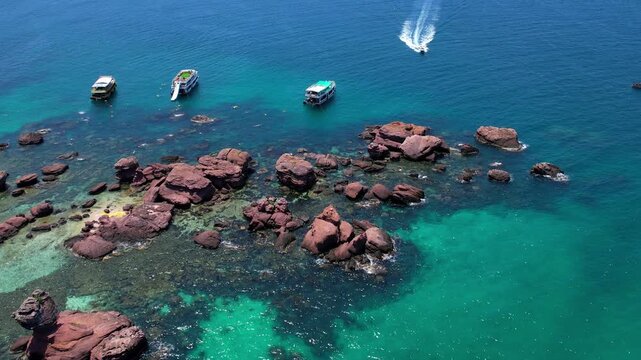 Stunning aerial drone video of Gam Ghi Island on Phu Quoc in south Vietnam with turquoise blue water and vivid coral reefs with tourists snorkeling and jumping off the boats on a hot sunny day