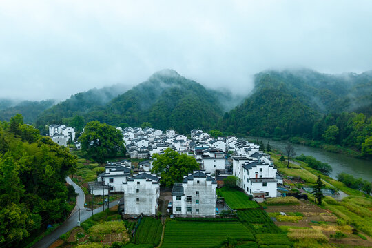 Aerial landscape of Huizhou Ancient City, She County, Anhui, China, displaying ancient white houses and green fields by a river amidst misty mountains