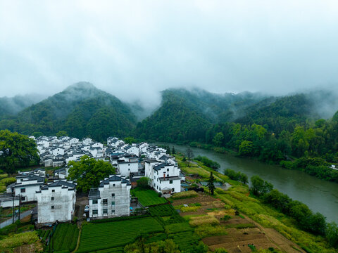 An aerial view reveals traditional white houses of Huizhou Ancient City in She County, Anhui, China, nestled by a winding river and lush misty mountains