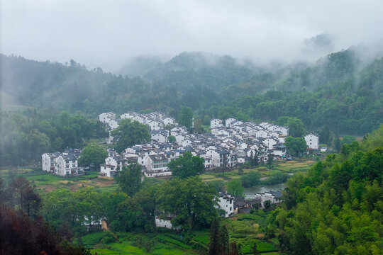 Traditional white houses of Huizhou Ancient City stand in the scenic green mountains of She County in Anhui province China during a beautiful morning with soft mist covering the landscape