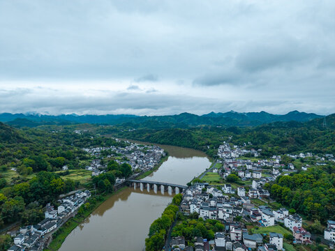 An aerial view captures the traditional architecture and historic bridge of Huizhou Ancient City located in She County of Anhui province in China surrounded by lush green mountains and a river